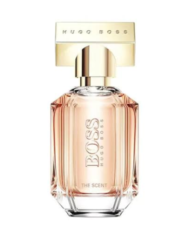 Hugo Boss The Scent Eau de Toilette bottle, featuring a faceted clear glass body filled with a peach-colored fragrance liquid, topped with a metallic gold cap and a gold rectangular logo plate.