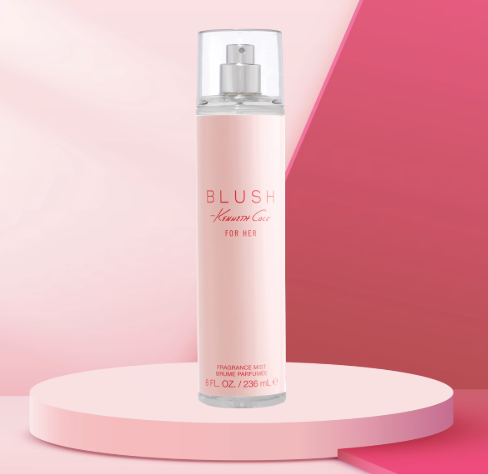 A bottle of Blush by Kenneth Cole For Her fragrance mist, presented on a pink cylindrical pedestal against a pink and magenta geometric background.