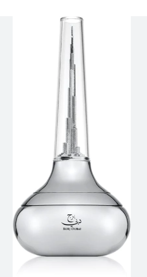 A clear glass perfume bottle with a wide rounded base and a long narrow neck, featuring a miniature metallic skyscraper model inside. The base is printed with the Burj Khalifa logo and the text 'BURJ KHALIFAH'.