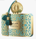 A perfume bottle by Isabella Moonlight featuring a turquoise and gold Moroccan-inspired design with intricate scrollwork, a spherical gold cap, and a teal tassel with gold accents.