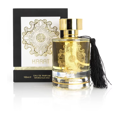 A bottle of Karat Eau de Parfum with a black tassel, displayed next to its black and white packaging box on a reflective white surface.