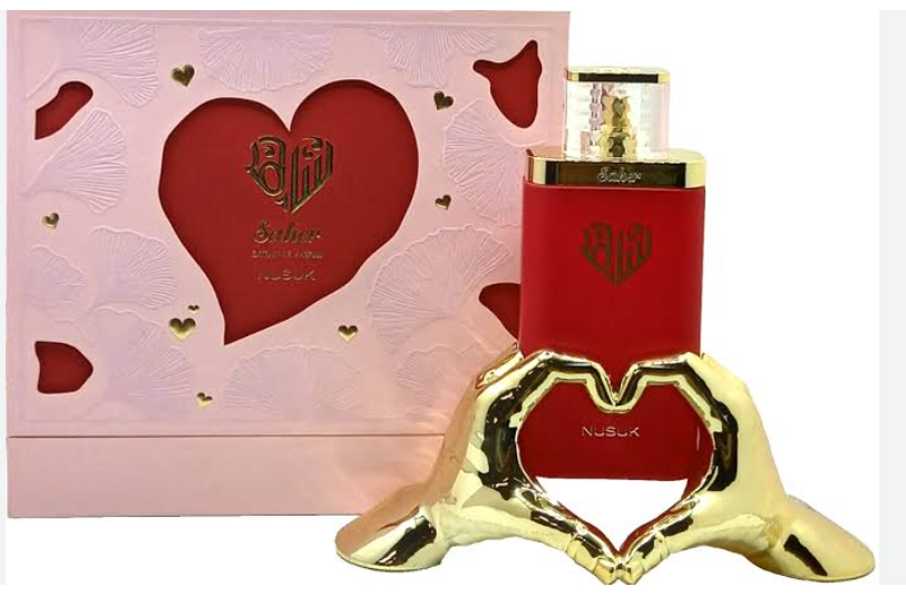 Nusuk Babur perfume bottle in red with gold accents, displayed in front of its pink gift box with a large red heart cutout, alongside a gold heart-shaped stand.