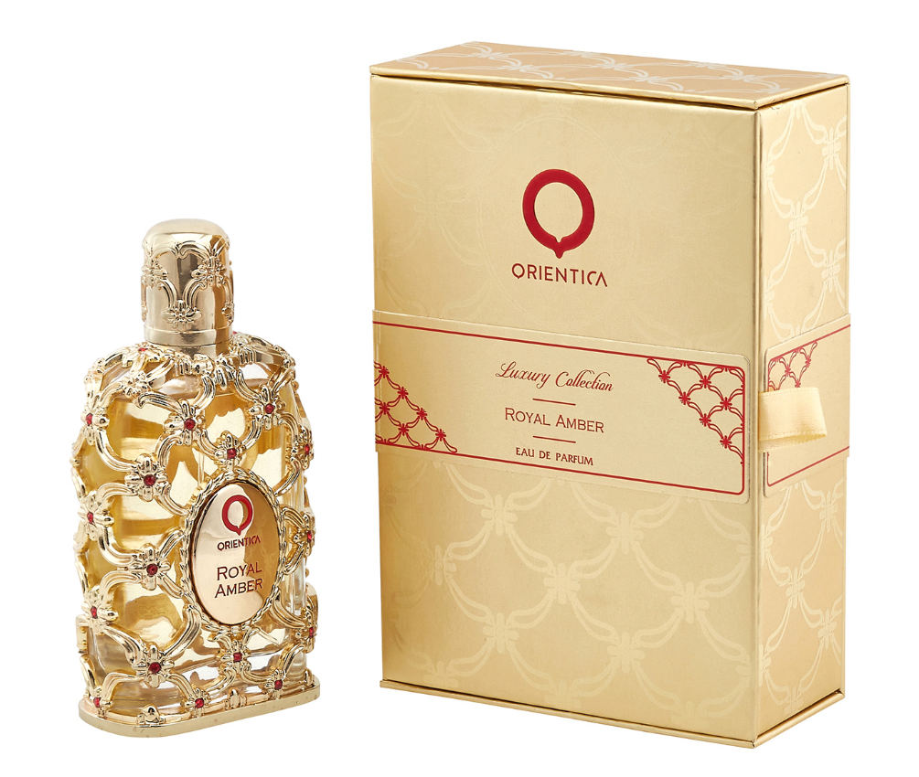 Orienta Royal Amber Eau de Parfum bottle next to its gold-colored packaging box, featuring a gold filigree design with red gem accents and the Orienta logo.