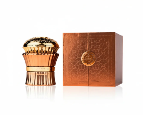A metallic rose gold perfume bottle with a textured, sculptural design stands next to its matching rose gold box with embossed patterns and a central circular seal, set against a clean white background with a subtle reflection.