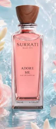 A rectangular glass perfume bottle filled with pink liquid, featuring a brown wooden cap and the text 'Surrati Since 2015' and 'Adore Me Eau de Parfum' on the front. The bottle is centered against a soft, icy blue background with water ripples and blurred pink flower petals.